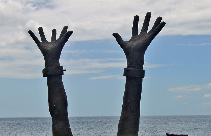 foto di mani  di una statua alzate al cielo con polsi liberi dalle catene